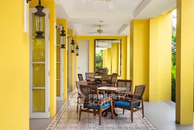 Charming outdoor patio with vibrant yellow walls and elegant wooden furniture, perfect for relaxation.