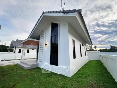 Modern white house with sleek design and lush green lawn under a cloudy sky.