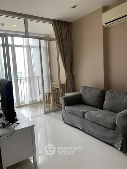 Modern living room with sleek sofa and large windows leading to a balcony, offering ample natural light.