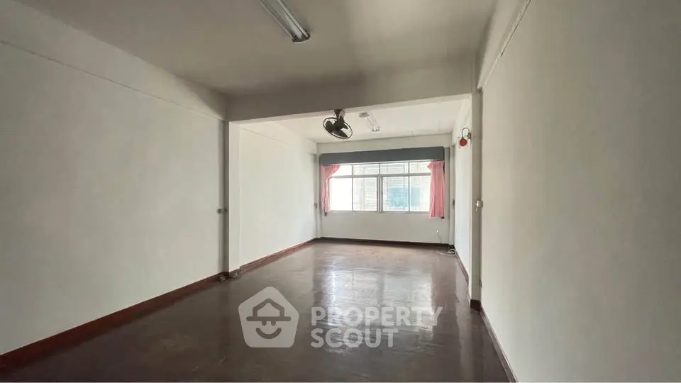 Spacious empty room with large window and wooden flooring, ideal for customization.