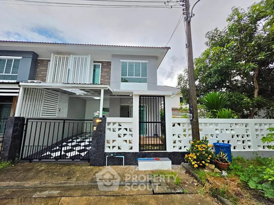 Charming two-story townhouse with modern facade and gated entrance, surrounded by lush greenery.