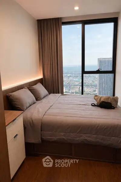 Modern bedroom with large window offering stunning city view, featuring cozy bed and elegant decor.