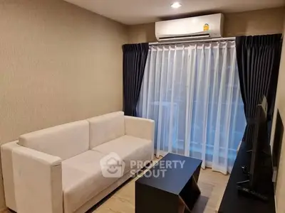 Modern living room with sleek sofa and large window draped with curtains, featuring a wall-mounted air conditioner.
