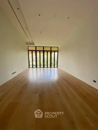 Spacious empty room with large windows and wooden flooring, ideal for customization.