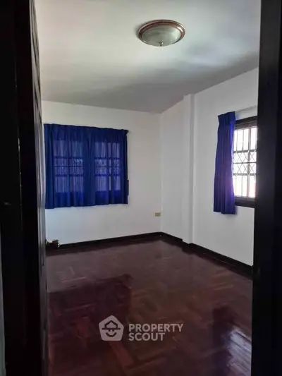 Spacious empty room with wooden flooring and blue curtains, ideal for customization.