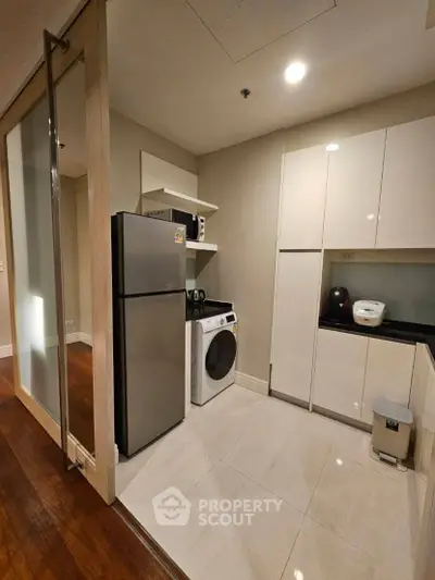 Modern kitchen with sleek appliances and ample storage space, featuring a fridge and washing machine.