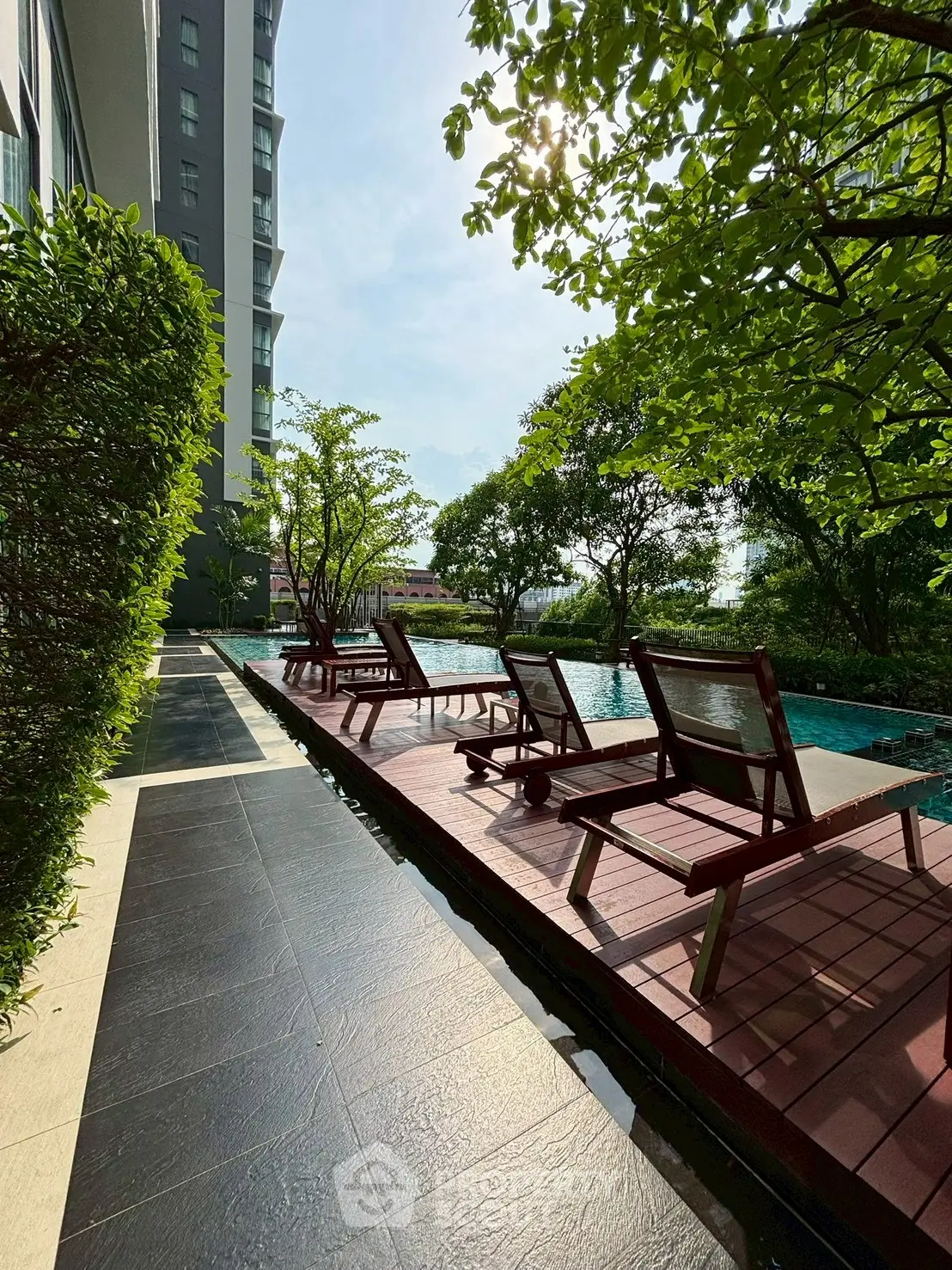 Luxurious outdoor pool area with sun loungers and lush greenery in modern residential complex.