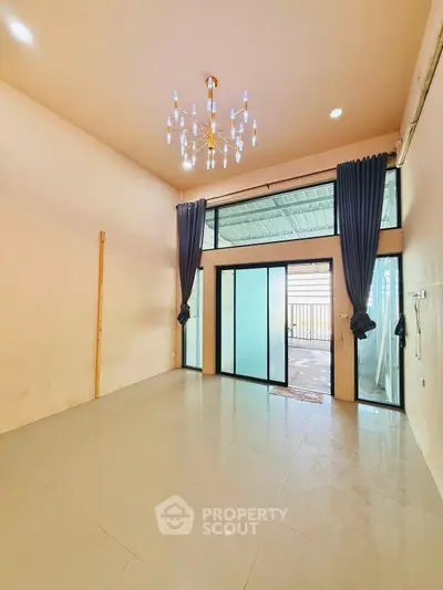 Spacious living room with high ceiling and elegant chandelier, featuring large windows and modern curtains.