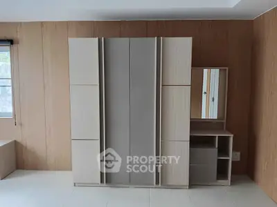 Modern bedroom with sleek wardrobe and vanity set against wood panel walls.