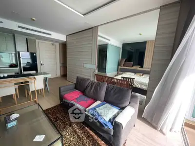 Modern open-plan living room with cozy sofa and dining area, featuring sleek kitchen appliances and stylish decor.