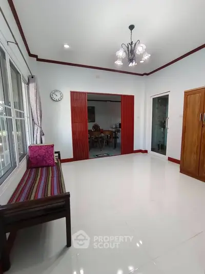 Spacious living room with elegant decor and natural light, featuring a stylish chandelier and wooden accents.