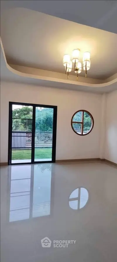 Spacious empty room with modern chandelier and large windows overlooking garden.