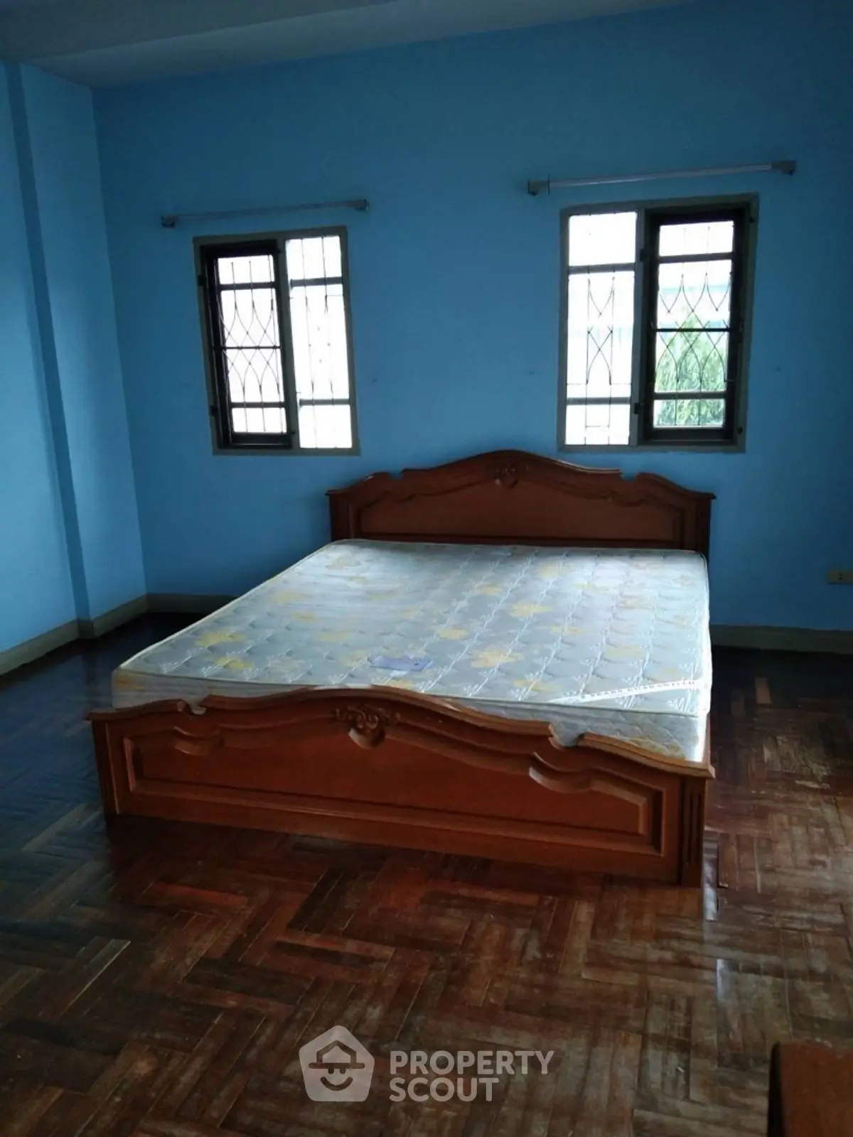 Spacious bedroom with wooden bed and blue walls, featuring parquet flooring and natural light.