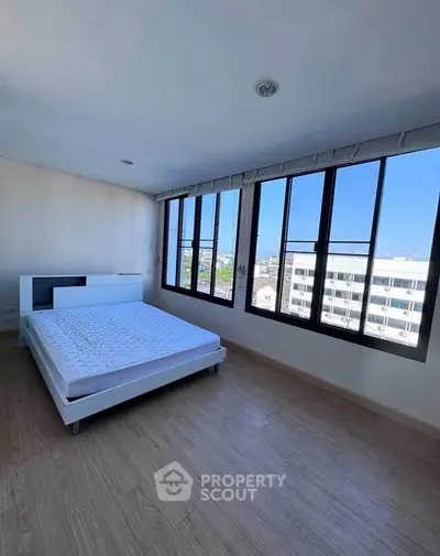 Spacious bedroom with large windows offering a stunning city view, featuring a modern bed and wooden flooring.
