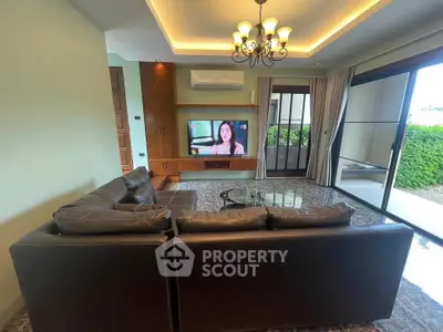 Spacious living room with modern decor, large TV, and sliding glass doors leading to a lush garden view.