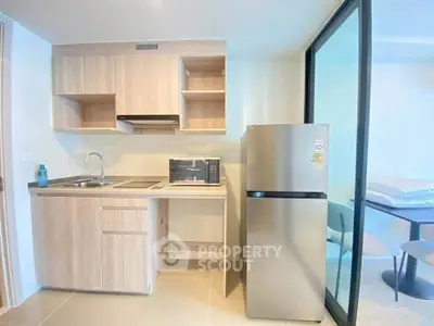 Modern compact kitchen with sleek cabinetry and stainless steel fridge in a bright apartment.