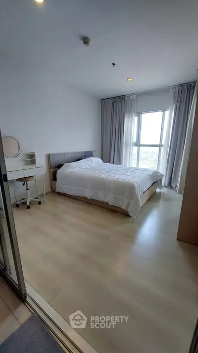 Spacious bedroom with large window offering natural light and modern furnishings in a high-rise apartment.