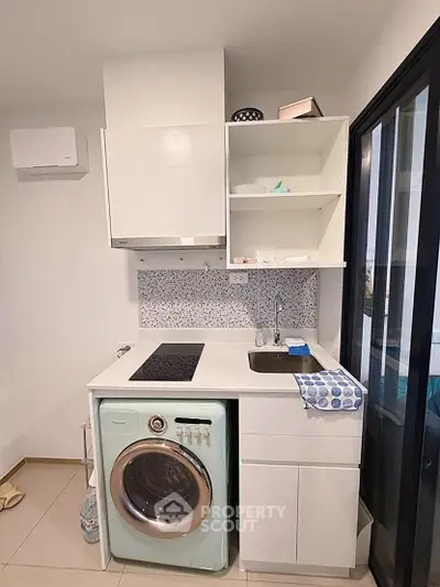 Compact kitchen with washing machine and modern cabinetry in a cozy apartment.