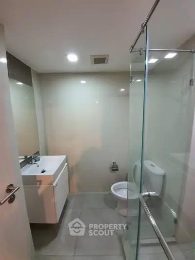 Modern bathroom with glass shower and sleek vanity in contemporary apartment.