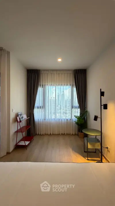 Spacious bedroom with large window and modern decor in a high-rise apartment.