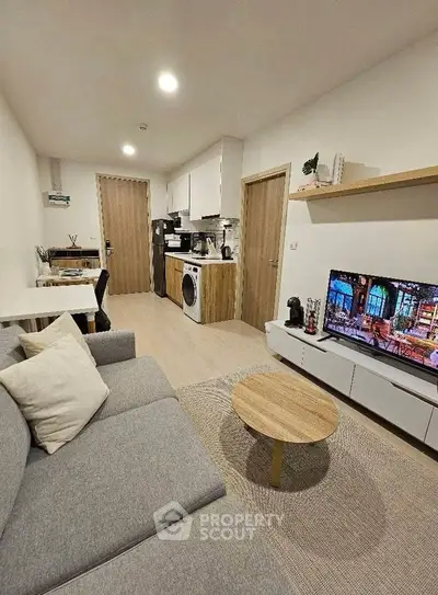 Modern living room with cozy gray sofa, TV, and compact kitchen area.