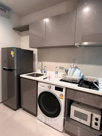 Modern kitchen with sleek cabinets, washing machine, fridge, and microwave in compact layout.