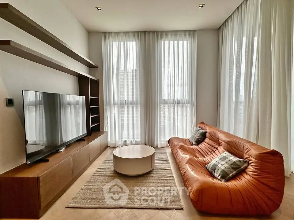 Modern living room with stylish sofa, large TV, and natural light from tall windows.