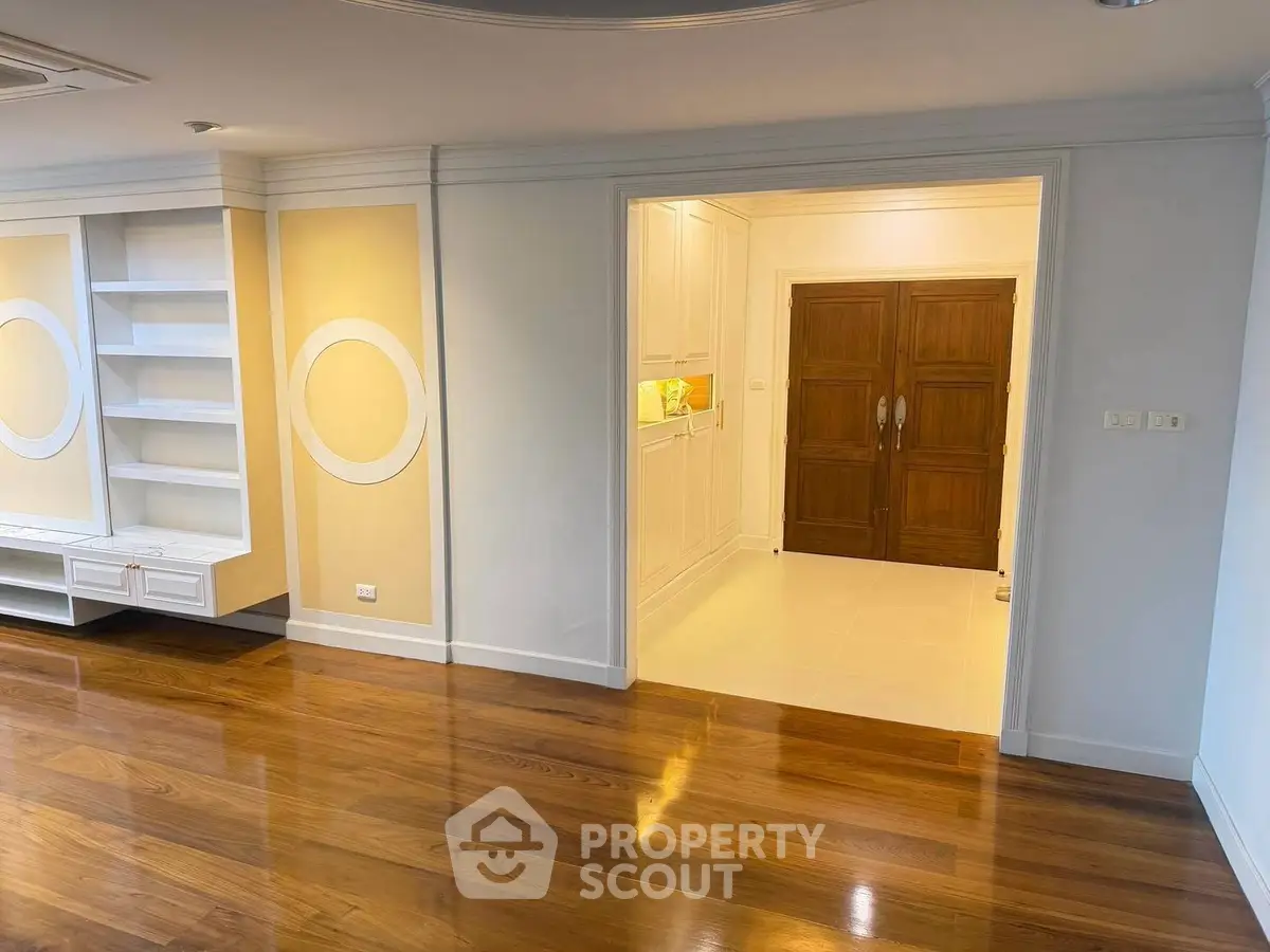 Spacious living area with elegant wooden flooring and built-in shelves, leading to a stylish entrance.