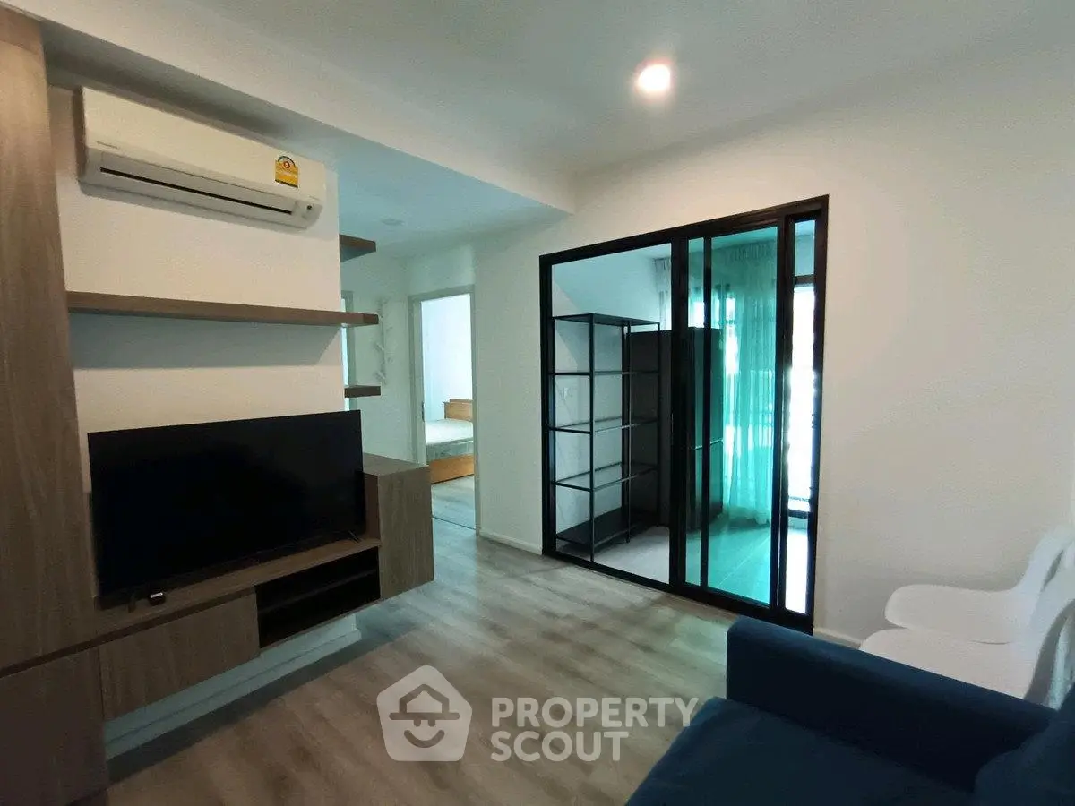 Modern living room with sleek design, featuring a TV unit and sliding glass doors leading to a bedroom.