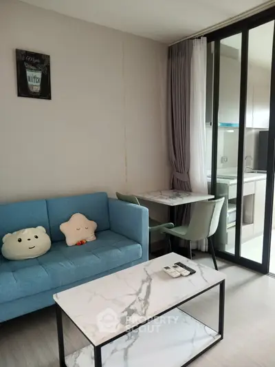 Modern living room with cozy blue sofa, marble coffee table, and open kitchen layout.