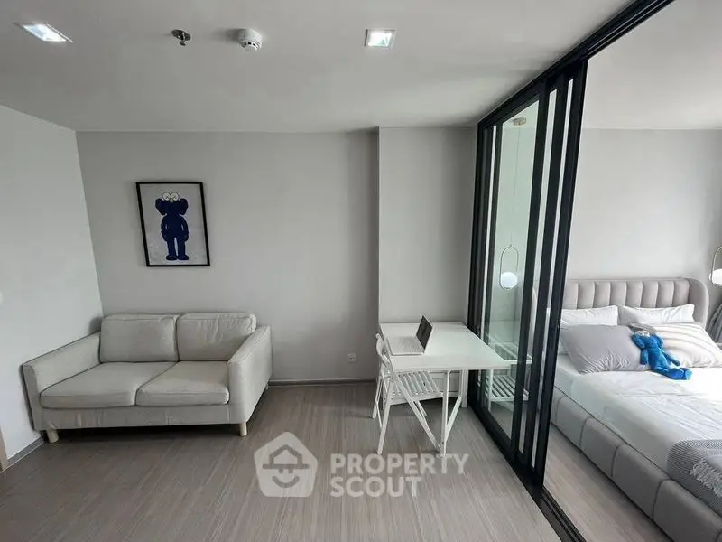 Modern apartment interior with cozy living room and stylish bedroom separated by glass wall.