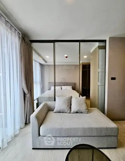 Modern bedroom with glass partition and cozy seating area, featuring elegant curtains and soft lighting.