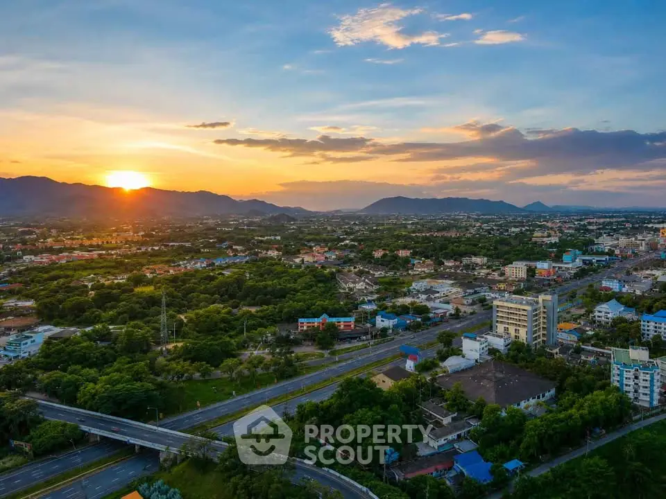 Stunning aerial view of a vibrant cityscape at sunset with lush greenery and distant mountains.