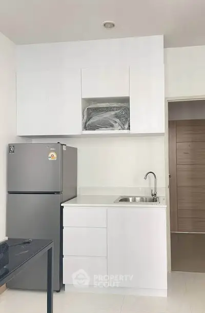 Modern kitchen with sleek white cabinets and stainless steel fridge in a compact layout.