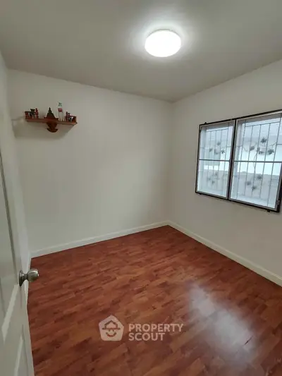 Spacious empty room with wooden flooring and bright window, ideal for customization.