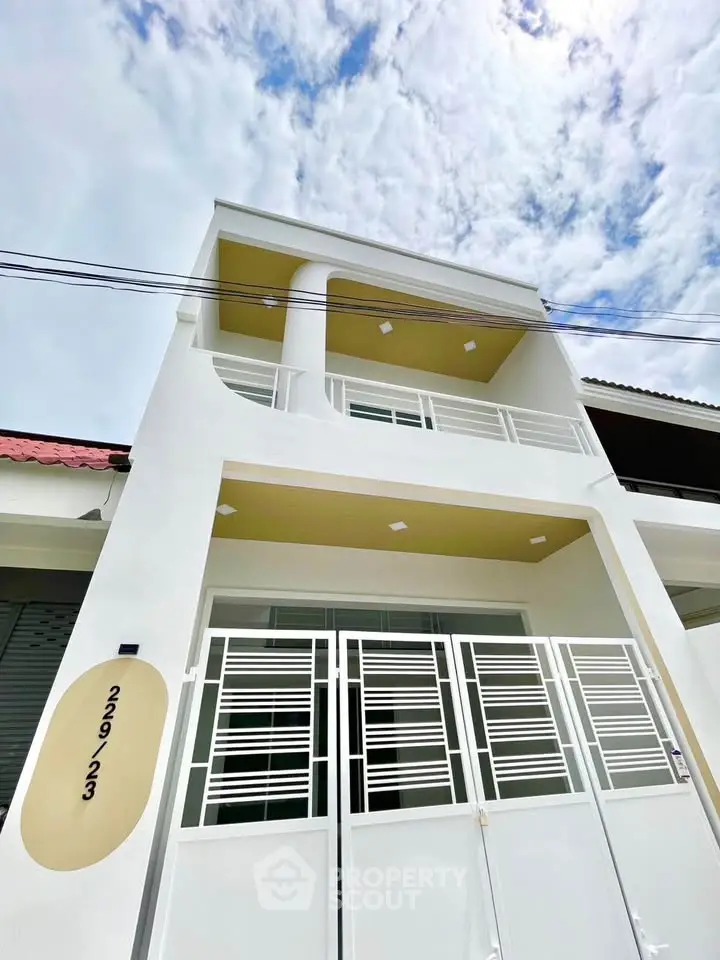 Modern white three-story building with sleek design and gated entrance under a bright sky.