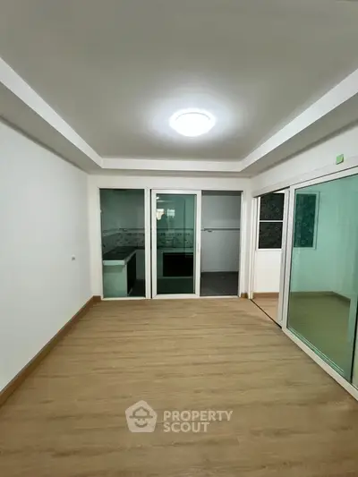 Spacious living room with wooden flooring and sliding glass doors leading to a kitchen area.