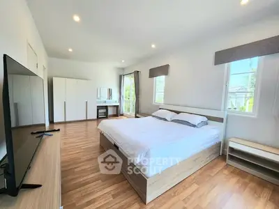 Spacious modern bedroom with wooden flooring and large windows for natural light.