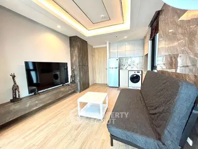 Modern living room with TV, sofa, and kitchen appliances in open layout.