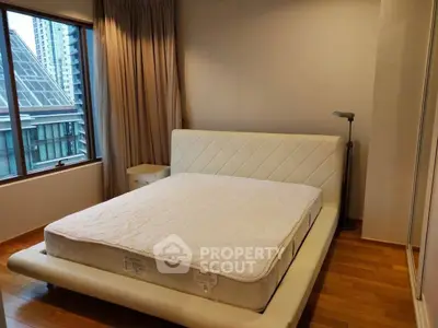 Modern bedroom with large window and city view, featuring a stylish bed and wooden flooring.