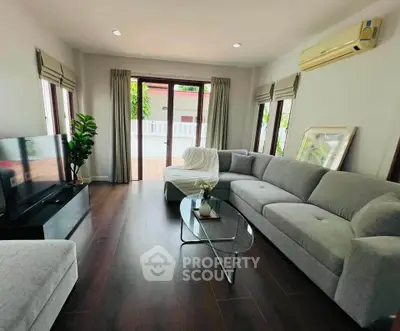 Spacious living room with modern gray sofa and glass coffee table, featuring large windows and wooden flooring.