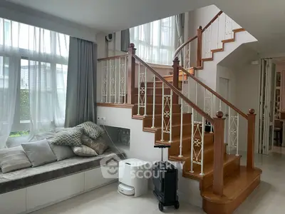 Elegant interior with wooden staircase and cozy seating area by large windows.