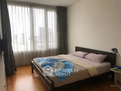 Spacious bedroom with large window and wooden flooring in modern apartment.