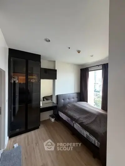 Cozy bedroom with modern furnishings and large window offering city views, perfect for urban living.