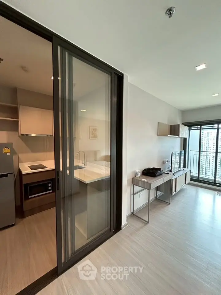 Modern apartment interior with open kitchen and spacious living area featuring large windows and balcony view.