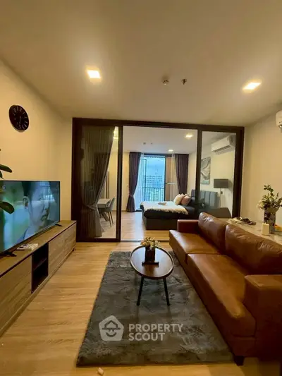 Modern living room with leather sofa and TV, open view to bedroom