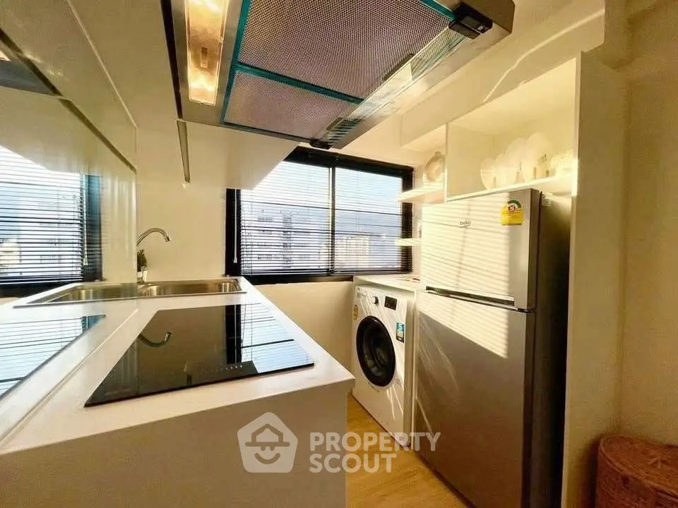 Modern kitchen with sleek appliances and natural light, featuring a washing machine and fridge.
