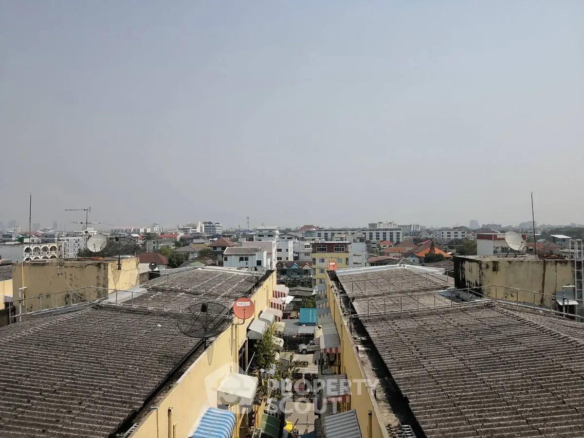 Panoramic view of urban residential rooftops with clear sky, showcasing cityscape and distant buildings.