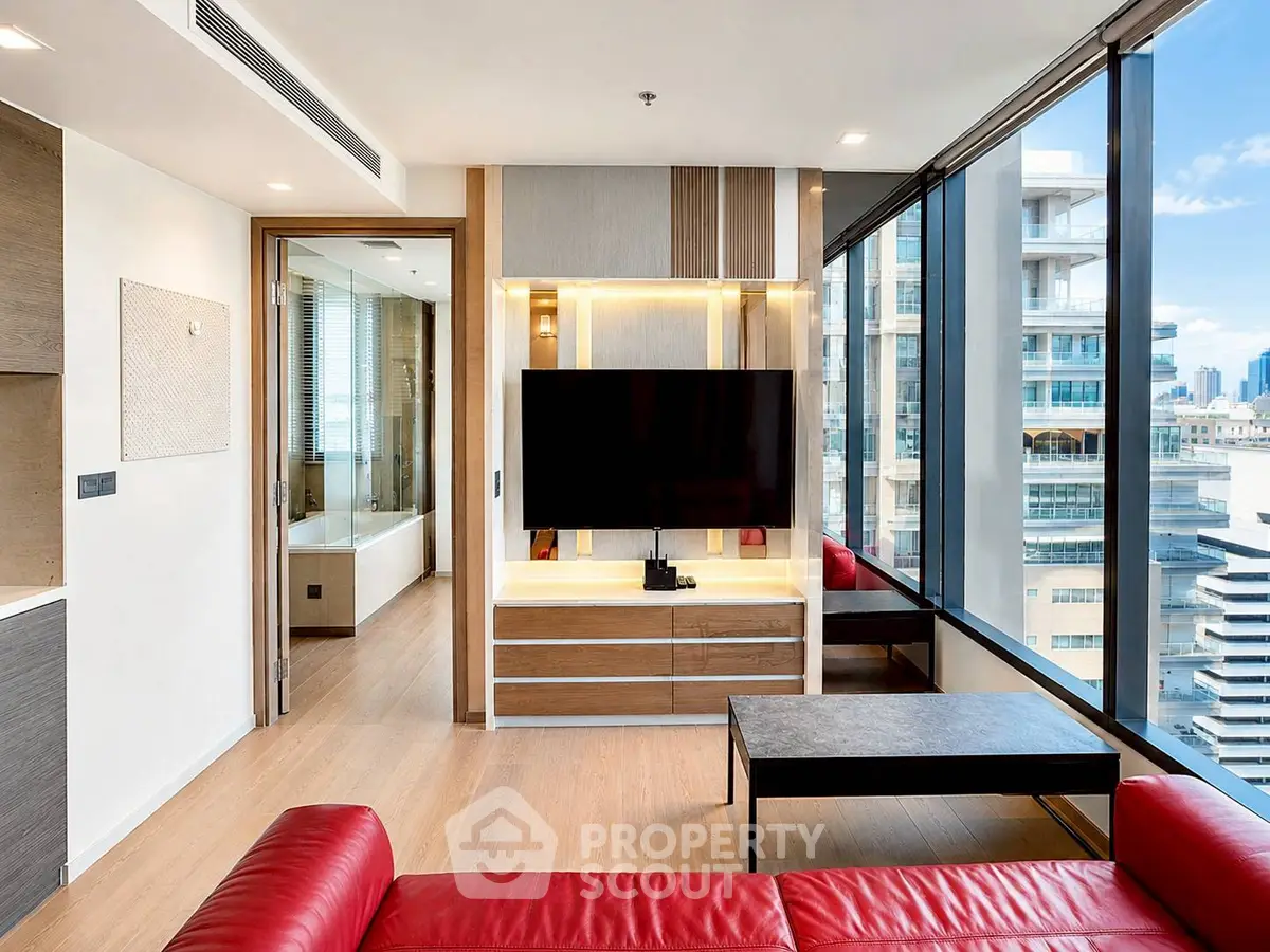 Modern living room with red sofa and large windows offering city views in a high-rise apartment.