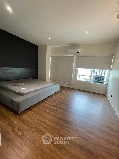 Spacious modern bedroom with sleek wooden flooring and large windows.